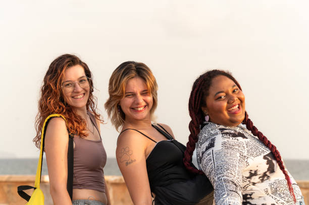 Three friends turning to the side and smiling at camera next to the sea