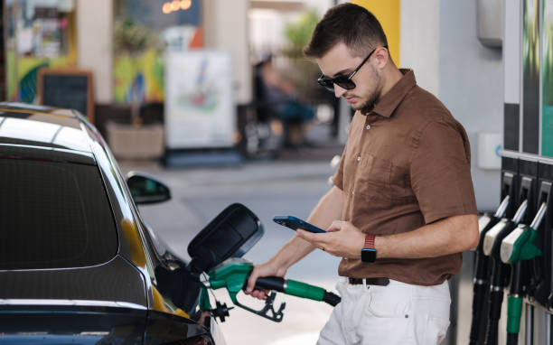 Man refueling his car on gas station and looking into his smartphone. Guy compares fuel prices in internet. Benzine. Luxury car stock photo