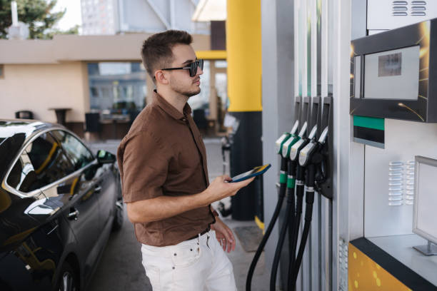istock Handsome young man refueling his luxury car and looking on the scoreboard while standing on self service gas station 2172110188