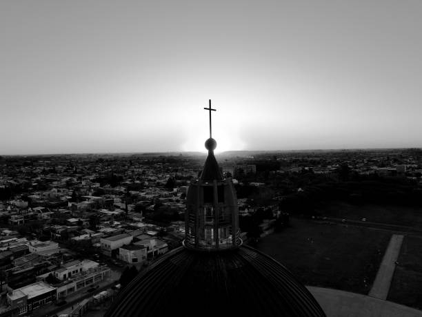 La cúpula del Santuario de San Nicolás se alza en contraste, donde la cruz de Cristo emerge en un cielo de sombras.\