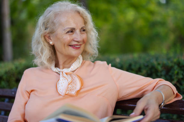 Shot of Senior Beautiful Woman Looking Away While Reading a Book in a Public Park
