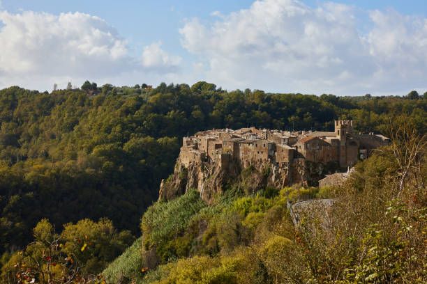Idyllic shot of medieval townscape of Calcata on volcanic cliff surrounded with lush green trees against cloudy sky during sunny day