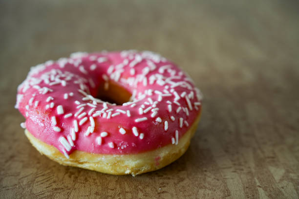 High angle view of a pink donut with crumbs on a white background