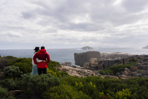 couple standing on a large rock looking at beach