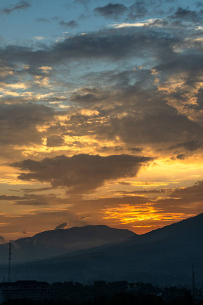This image captures a beautiful sunset over a mountain range. The sky is a vibrant orange and yellow, with cloudy sky. The sun is setting behind the mountains, casting long shadows over the landscape.