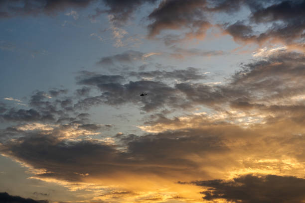 istock This image captures a beautiful sunset above the clouds and a helicopter passing by. The sky is bright orange and yellow, with an overcast sky. dramatic sunset landscape concept 2172154764