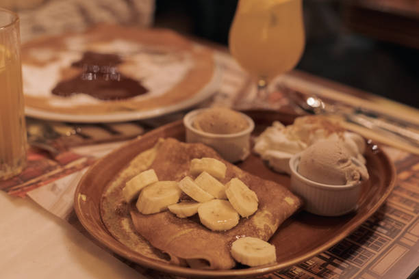 Appetizing view of a hot pancake with pieces of fresh banana and ice cream in a dish on a table in an evening restaurant, close-up side view. Treat time concept.