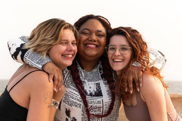 Close-up of three diverse young women laugh as they affectionately hug