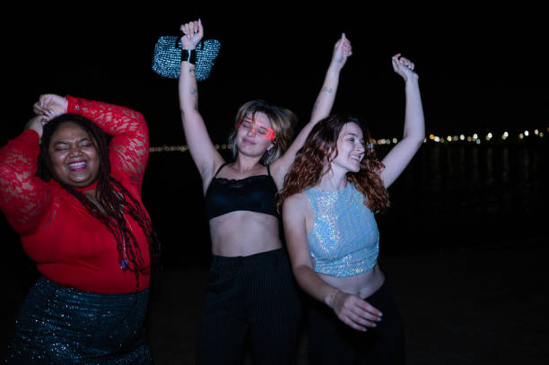 Multi-ethnic young excited women dancing free at beach night party