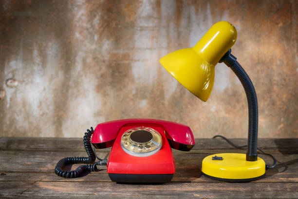 A table lamp and a red vintage phone on an old wooden table against a shabby background