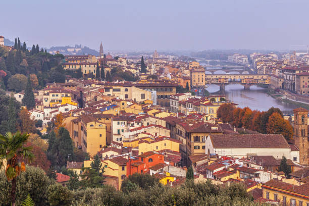 In the Florence cityscape, the Ponte Vecchio spans the Arno River in the distance, its medieval charm visible amid the backdrop of old houses and rooftops. The bridge adds a historic touch to the scene, while the surrounding architecture of timeworn buildings, rooftops and narrow streets paints a picture of timeless elegance and character.