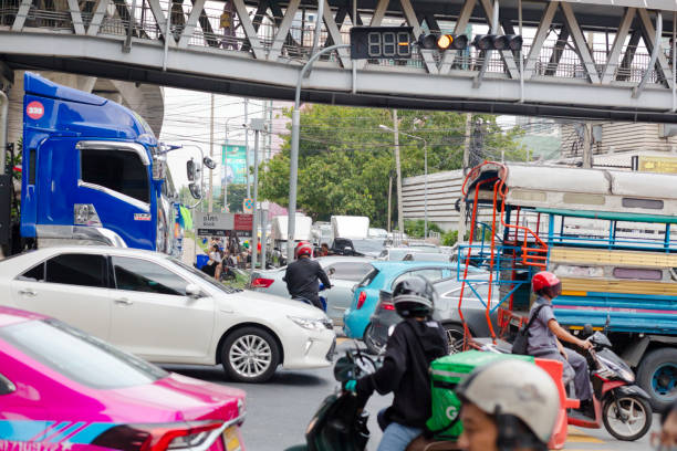 Traffic jam chaos at junction in Bangkok - scene is at intersection of Thanon Asok and Kamphenpet Road opposite to Makkasan airport railway station. In background is pedestrian footbridge with walking people. Between vcars are motorcycle drivers. And in point of view are old railway tracks from old Makkasan sttaion leading to east