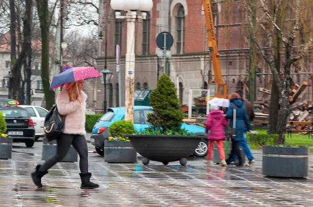 Timisoara, Romania - March 23, 2016: Woman walking on the street in the rain with an umbrella in hand. Motion blur. Real people.