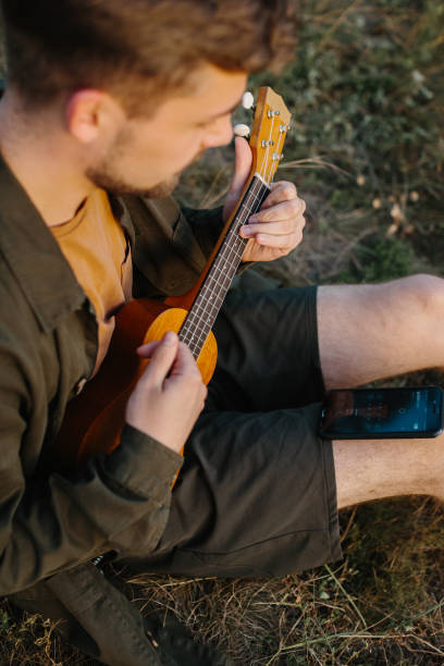 istock A young man plays the ukulele while sitting in a pine forest at sunset. 2172189561