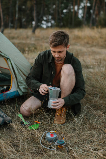 istock A young man prepares coffee on a camping stove near a tent. 2172189636