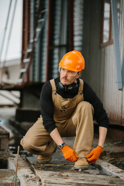 istock A worker in overalls and a protective helmet ties shoelaces at a construction site. 2172206875