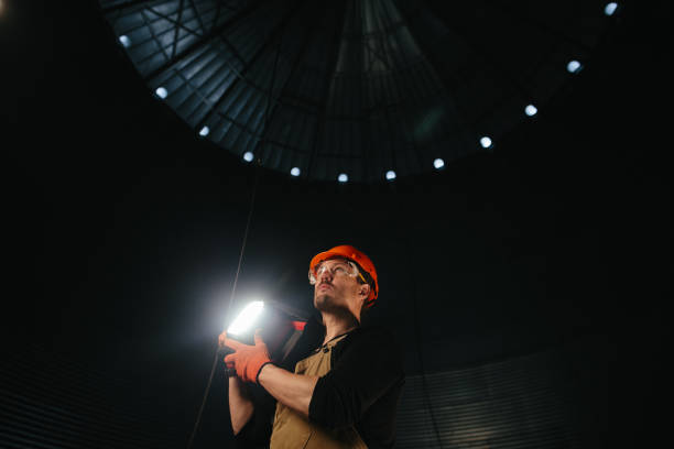 istock Male worker in safety helmet with flashlight in hands inside storage tank. Inside the grain silo. 2172206893