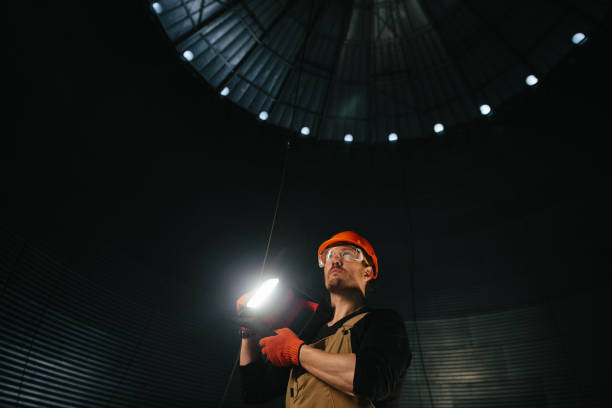 istock Male worker in safety helmet with flashlight in hands inside storage tank. Inside the grain silo. 2172206896