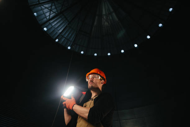 Male worker in safety helmet with flashlight in hands inside storage tank. Inside the grain silo.