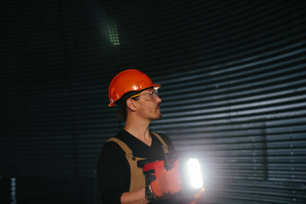 Male worker in safety helmet with flashlight in hands inside storage tank. Inside the grain silo.