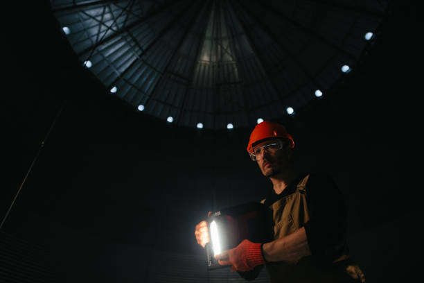 istock Male worker in safety helmet with flashlight in hands inside storage tank. Inside the grain silo. 2172206945