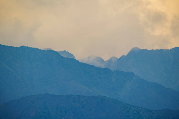 Distant mountain peaks partially obscured by mist during sunrise, creating a tranquil and atmospheric scene.