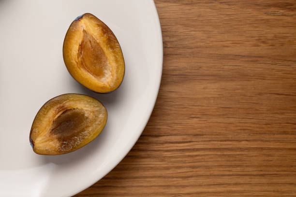 istock Halved plums on white plate and wooden surface. 2172213880