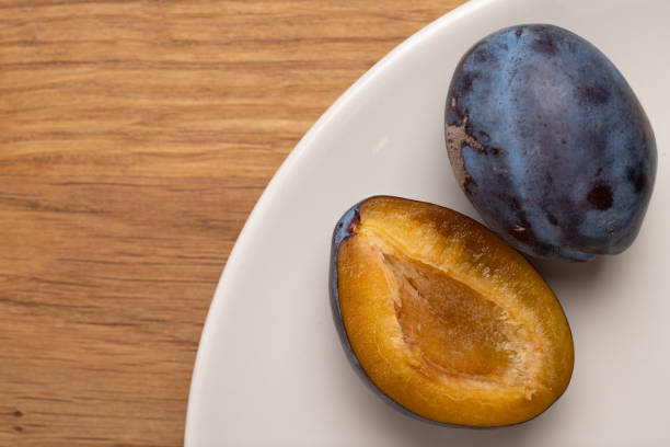 Whole and halved plum on white plate.