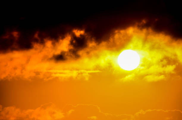 A sun is shining through the clouds on a cloudy day. The sun is yellow and the sky is dark