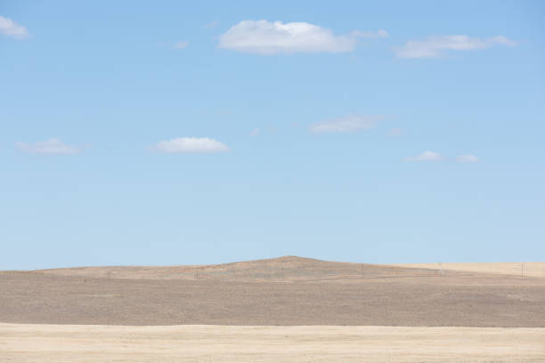 Expansive grasslands under a bright blue sky with scattered clouds. Small group of people in the distance. Isalo National Park, Madagascar.