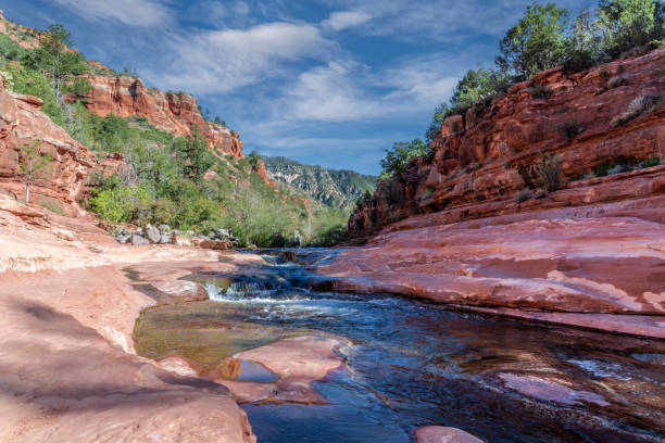 Oak Creek winds its way through the striking red rocks of Slide Rock State Park near Sedona, Arizona, USA. Once a historic apple orchard, this natural oasis now invites visitors to cool off in its crystal-clear waters amid the vibrant sandstone landscape.