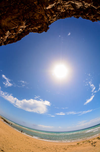 A beautiful blue sky with a sun shining brightly. The sun is in the middle of the sky and the beach is in the background