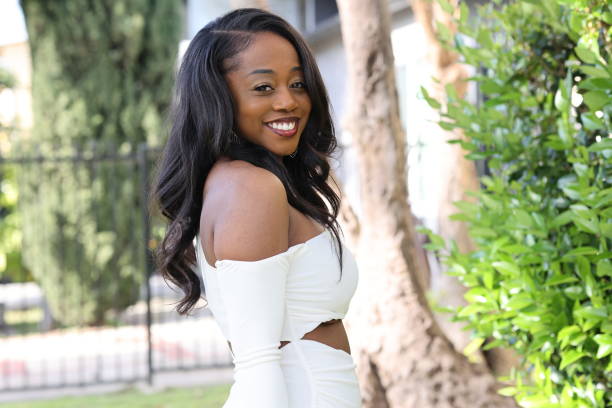 Woman smiling in white dress. Woman standing outside wearing off-the-shoulder white dress with long black hair. Looking at camera smiling with trees in the background during the day. straight-hair stock pictures, royalty-free photos & images