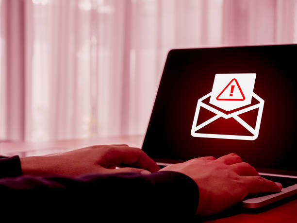 istock SMS spam, fake text message phishing scammer concept. Warning alert icon in opened envelope, e-mail hacked, scam malware spreading virus on laptop computer screen while man checking Email on website. 2172273901