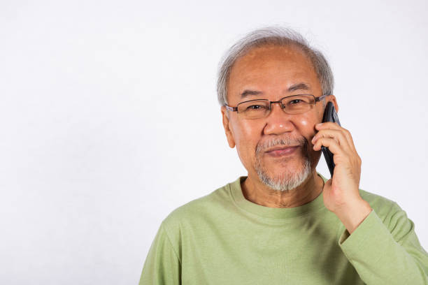 Portrait Asian smiling old man with glasses while talking on his cell phone studio shot isolated on white background, happy senior man calling to someone with mobile phone