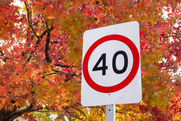 Road sign, speed limit, 40 km against the background of red and yellow autumn trees close-up, symbolic Road sign, speed limit, 40 km against the background of red and yellow autumn trees close-up, symbolic. High quality photo speed limit sign australia stock pictures, royalty-free photos & images