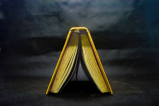 Open Quran book with golden edges on dark background, showcasing intricate Arabic script, symbolizing Islamic faith and spirituality