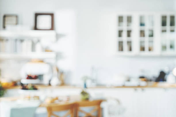 Interior view of a modern Scandinavian-style kitchen with clean lines, light wood surfaces, and a minimalist layout. The space features white upper cabinets, dark lower units, a soft yellow backsplash, and a compact dining area with black chairs and pendant lighting. Ideal for visuals focused on simple living, Nordic design, home organization, and contemporary lifestyle.