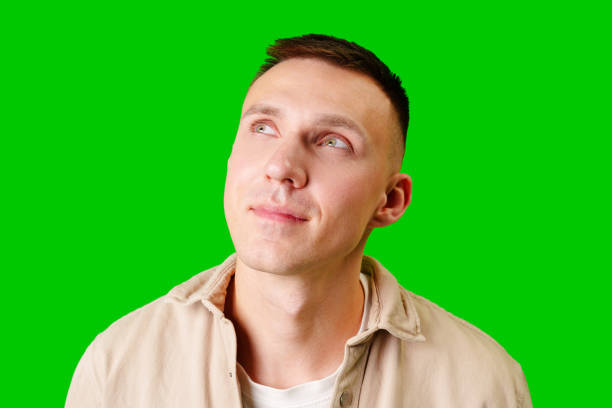 istock Young Man in Casual Attire Posing Thoughtfully Against a Bright Green Background 2172298639