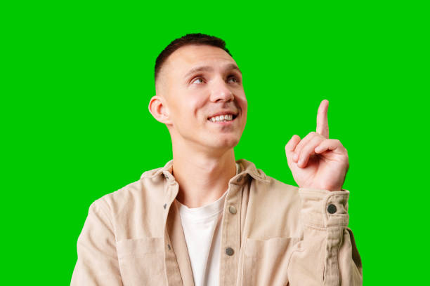 istock Young Man Pointing Upward While Smiling Against a Bright Green Background 2172299467