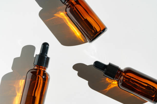 istock Arranged Amber Glass Bottles With Droppers on White Surface Accentuated by Shadows in Bright Light 2172300496