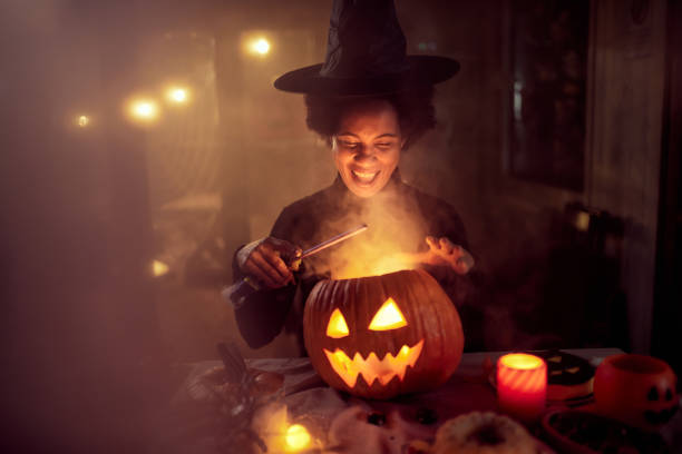Happy black witch casting spells on Jack O' Lantern during Halloween.