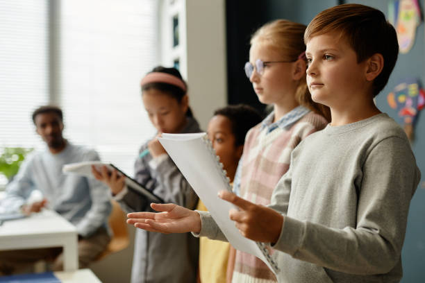 Boy Standing in Line Holding Exercise Book during Lesson at School