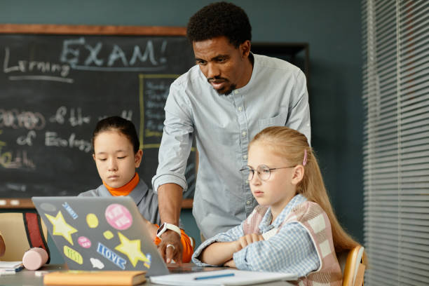 istock Male Teacher Helping Girl with Using Laptop to Study in Classroom 2172310406