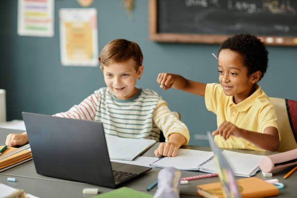 istock Smiling Black Boy Watching Video on Laptop with Classmate Studying in Classroom 2172310412