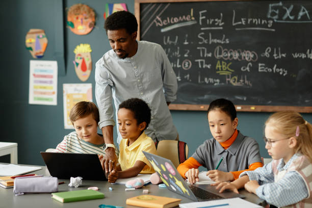 istock Children Using Laptops at Desk while Male Teacher Helping Kids in Classroom 2172310414