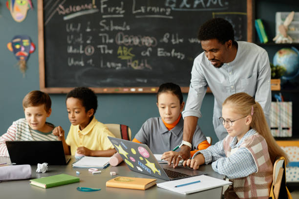 istock Male Teacher Helping Students with Using Laptop in Classroom 2172310419