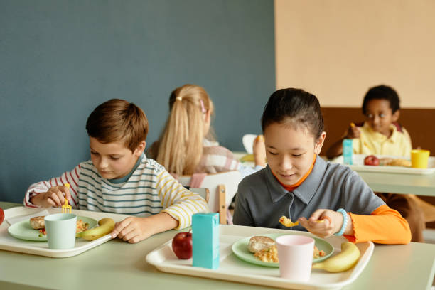 istock Primary School Children Sitting at Table Eating Lunch in Cafeteria 2172310459