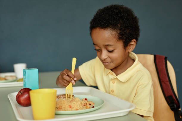 istock Black Boy Sitting at Table Enjoying Eating Lunch in School Cafeteria 2172310467