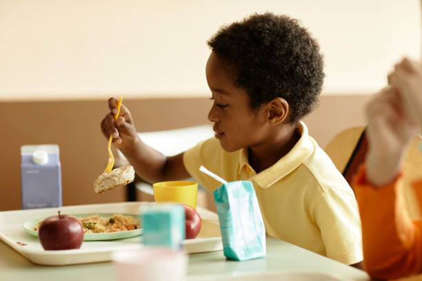Smiling Black Boy Sitting at Table Eating Lunch in School Cafeteria